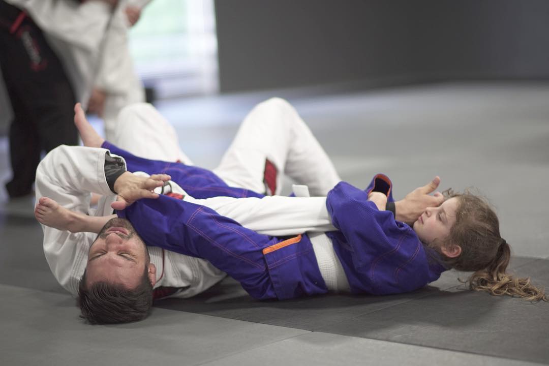 Young girl grappling with a man on the floor in martial arts uniforms