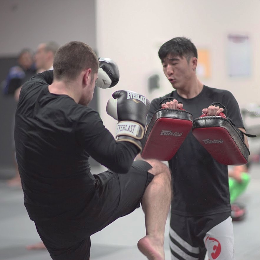 Man practicing muay thai with another man holding strike pads