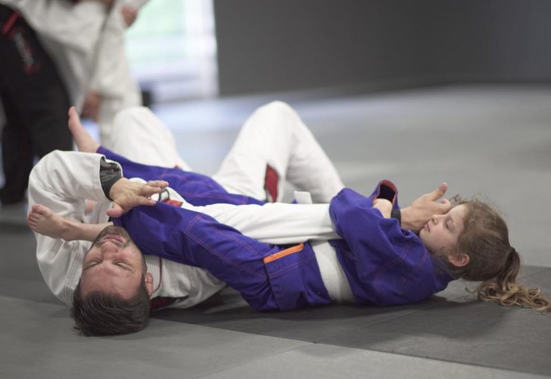 Young girl grappling with a man on the floor in martial arts uniforms