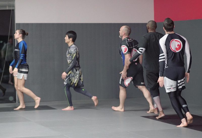 Adult martial arts students jogging around a mat