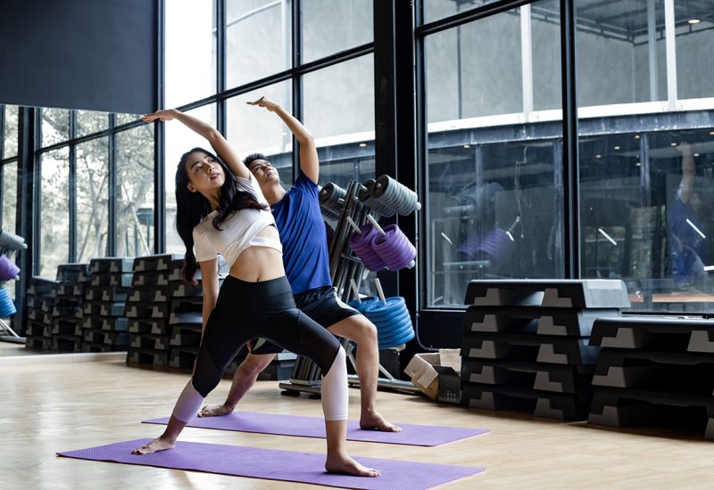 Young woman and young man standing yoga on the yoga mat in exercise room with copy space. Young couples with exercise by doing yoga together in indoor. Concept of exercise with yoga.